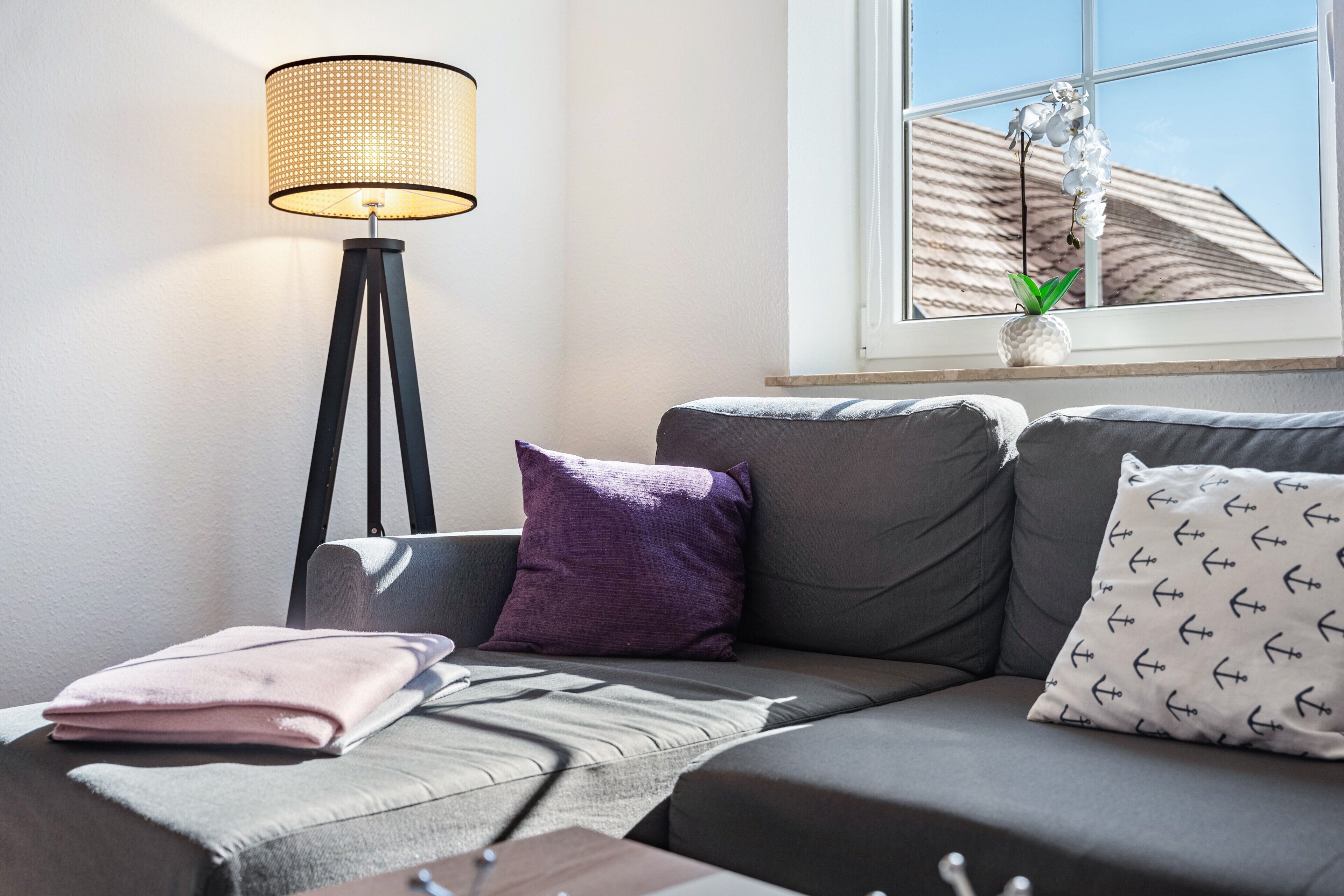 Un salon moderne avec un canapé, une lampe sur pied et une fenêtre agrémentée d’une plante.