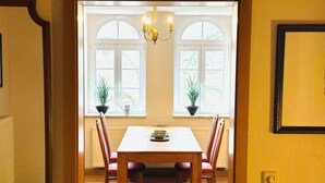 Un área de comedor con una mesa y sillas de madera, dos plantas en macetas, una araña y una ventana con vistas.