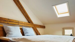 Un dormitorio con techo inclinado, tragaluces, cabecera de madera y cama con ropa blanca.