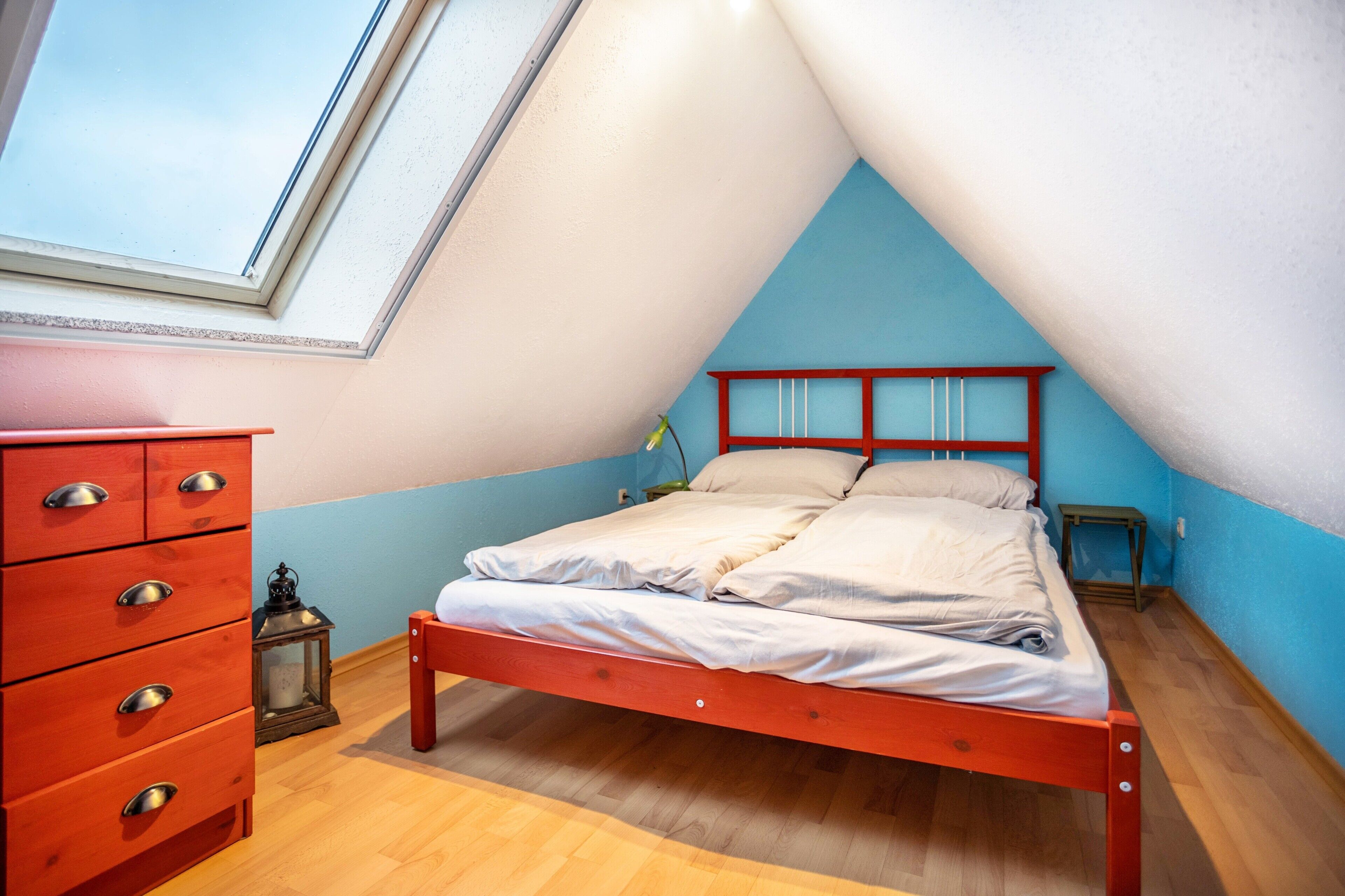 A bedroom with a sloped ceiling, a wooden bed frame, a dresser, and a nightstand.