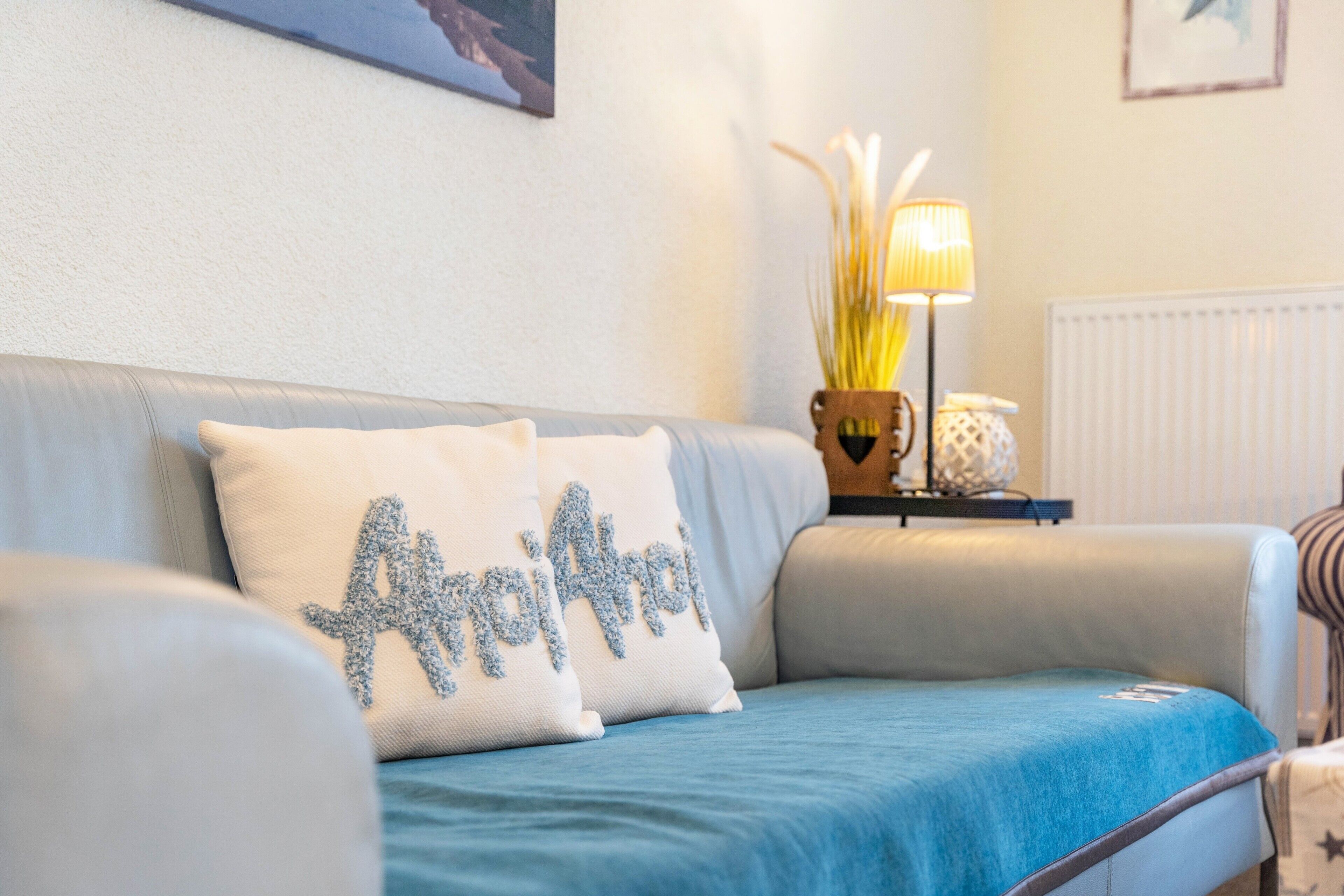 Un canapé recouvert d’une housse bleue, agrémenté de deux coussins, une lampe et un vase avec des plantes.