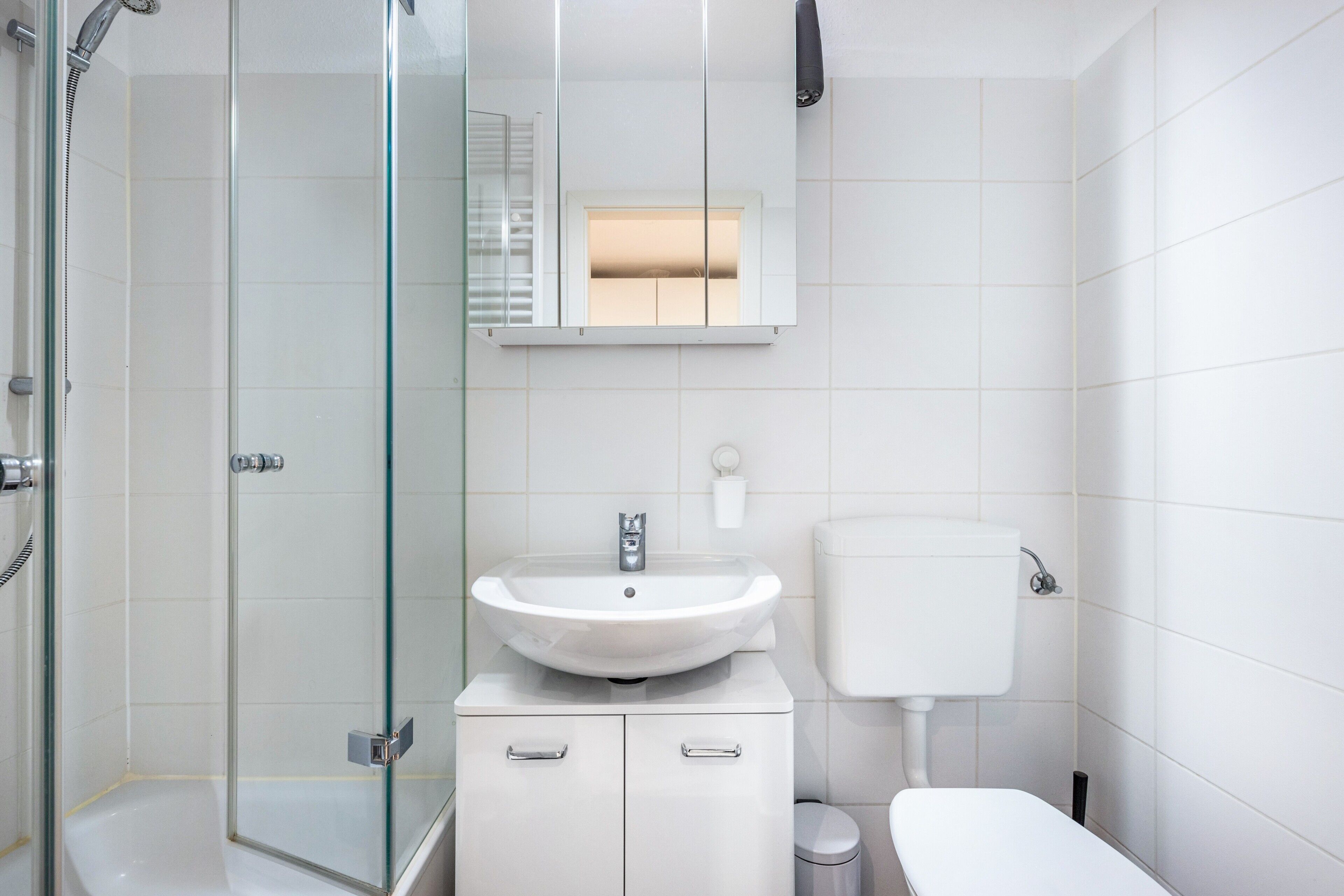 A modern bathroom with a glass shower enclosure, a white sink with a mirror above it, and a toilet.