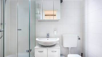 A modern bathroom with a glass shower enclosure, a white sink with a mirror above it, and a toilet.