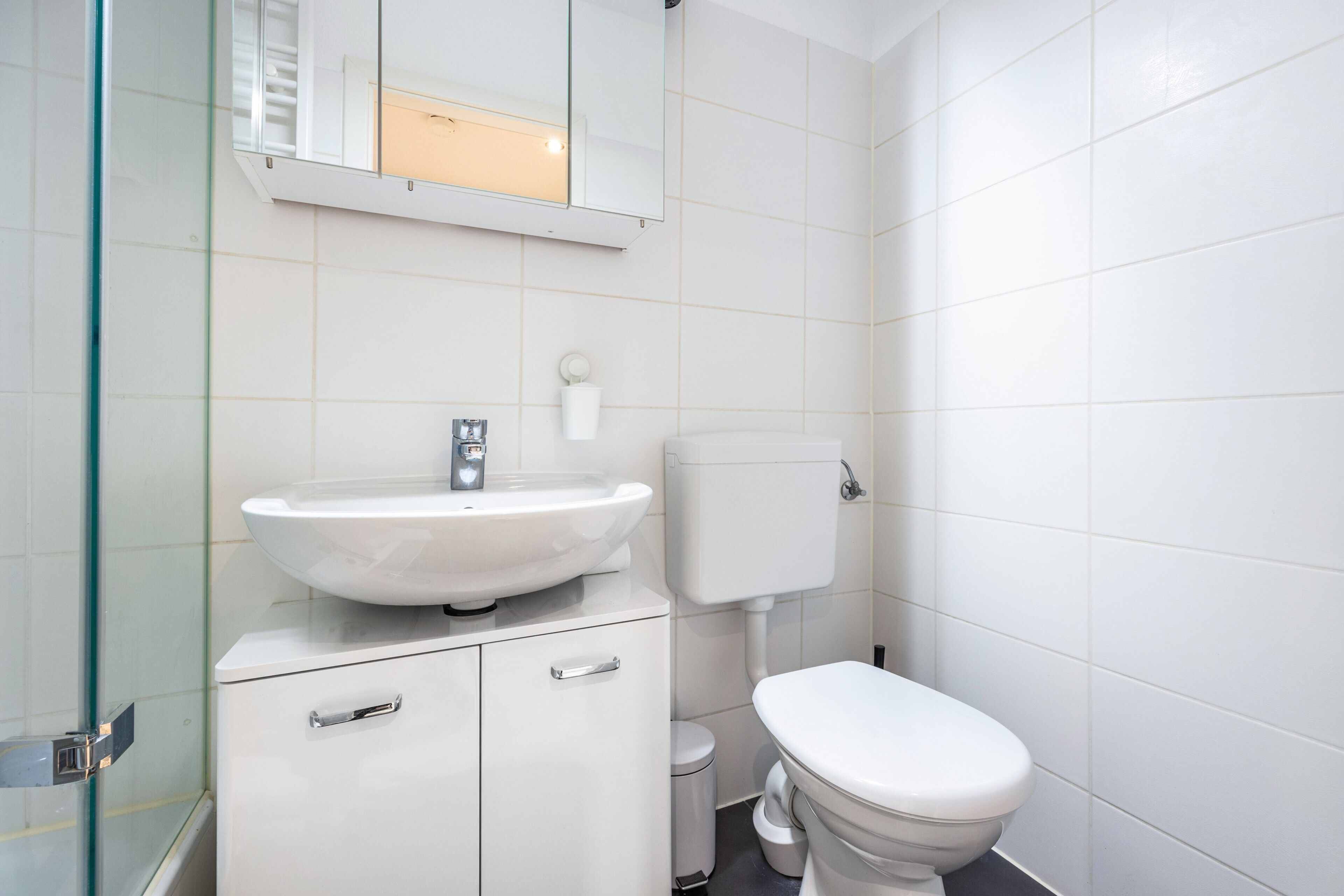 A bathroom with a white sink, toilet, and a glass shower enclosure.