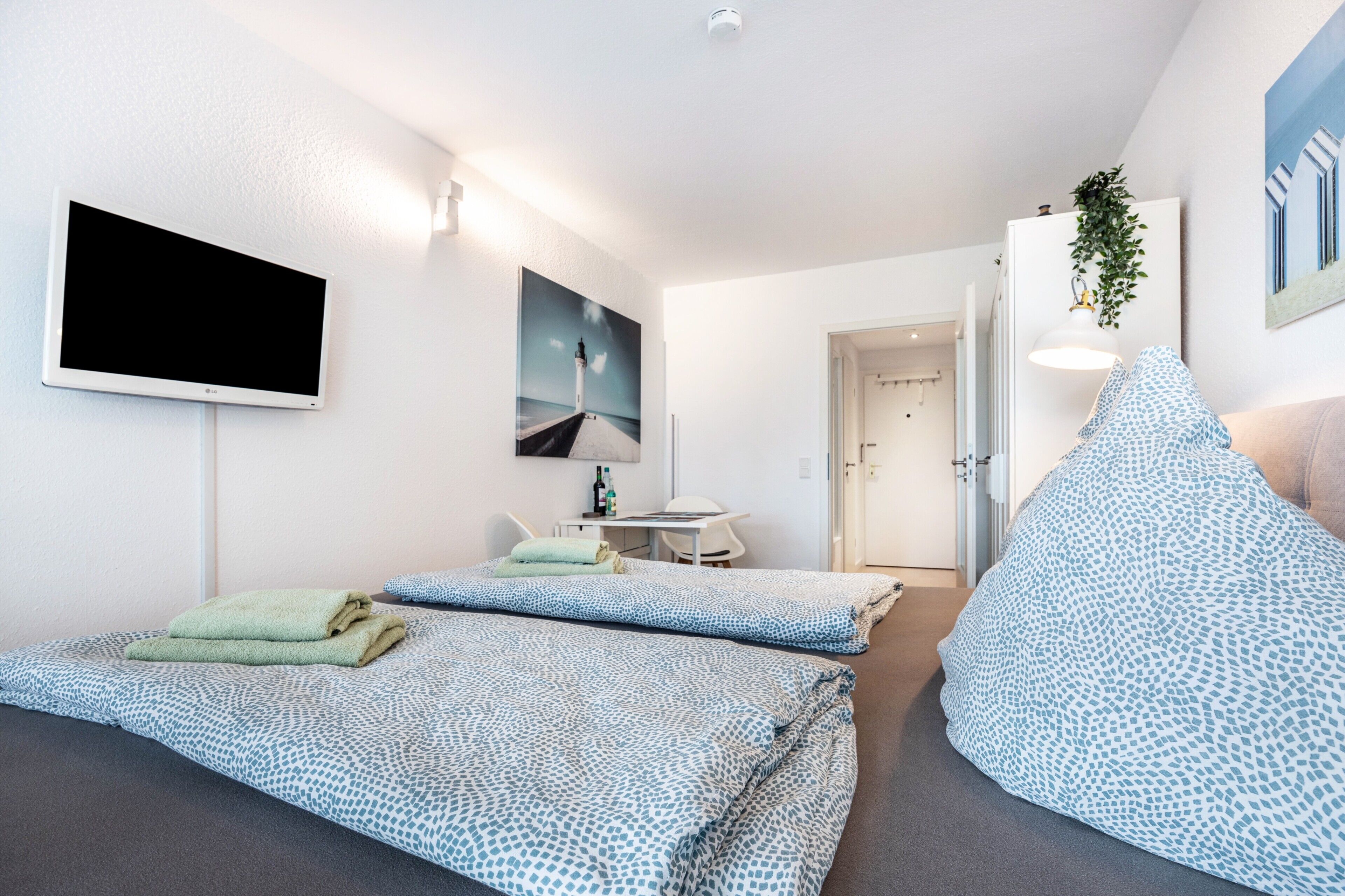 Ein modernes Zimmer mit zwei Betten, einem Schreibtisch, einem Flachbildfernseher und einer Tür zu einem weiteren Raum.
