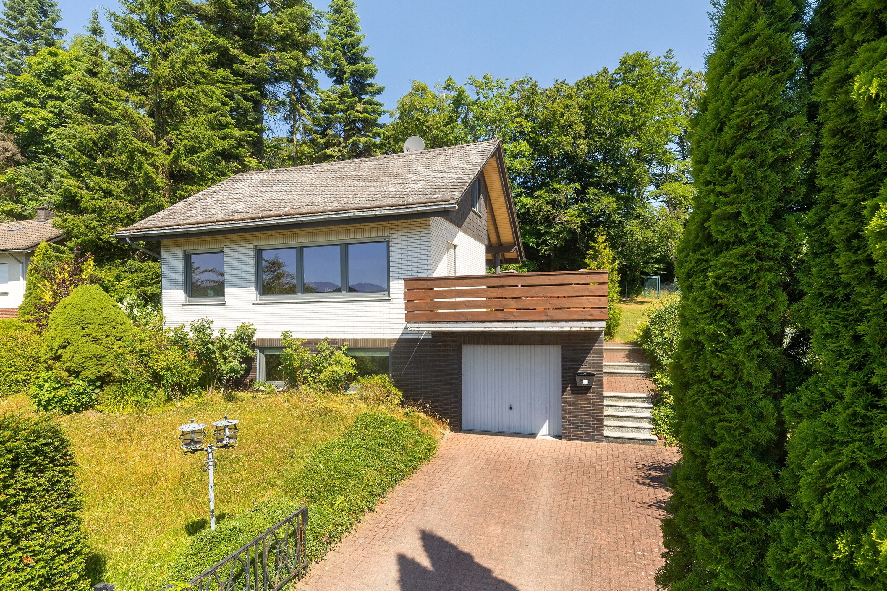 A two-story house with a garage, surrounded by greenery and trees.