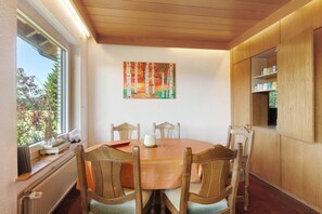 Un coin repas avec une table ronde, des chaises en bois, un tableau au mur et une fenêtre donnant sur les arbres.