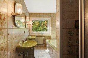 Une salle de bain avec deux lavabos, une baignoire et une fenêtre donnant sur les arbres.