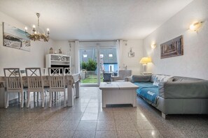 A living room with a dining table, chairs, a sofa, a coffee table, and a view through a glass door to the outside. - Holiday Home 'Ostsee' with Private Terrace, Private Garden and Wi-Fi (Pruchten)