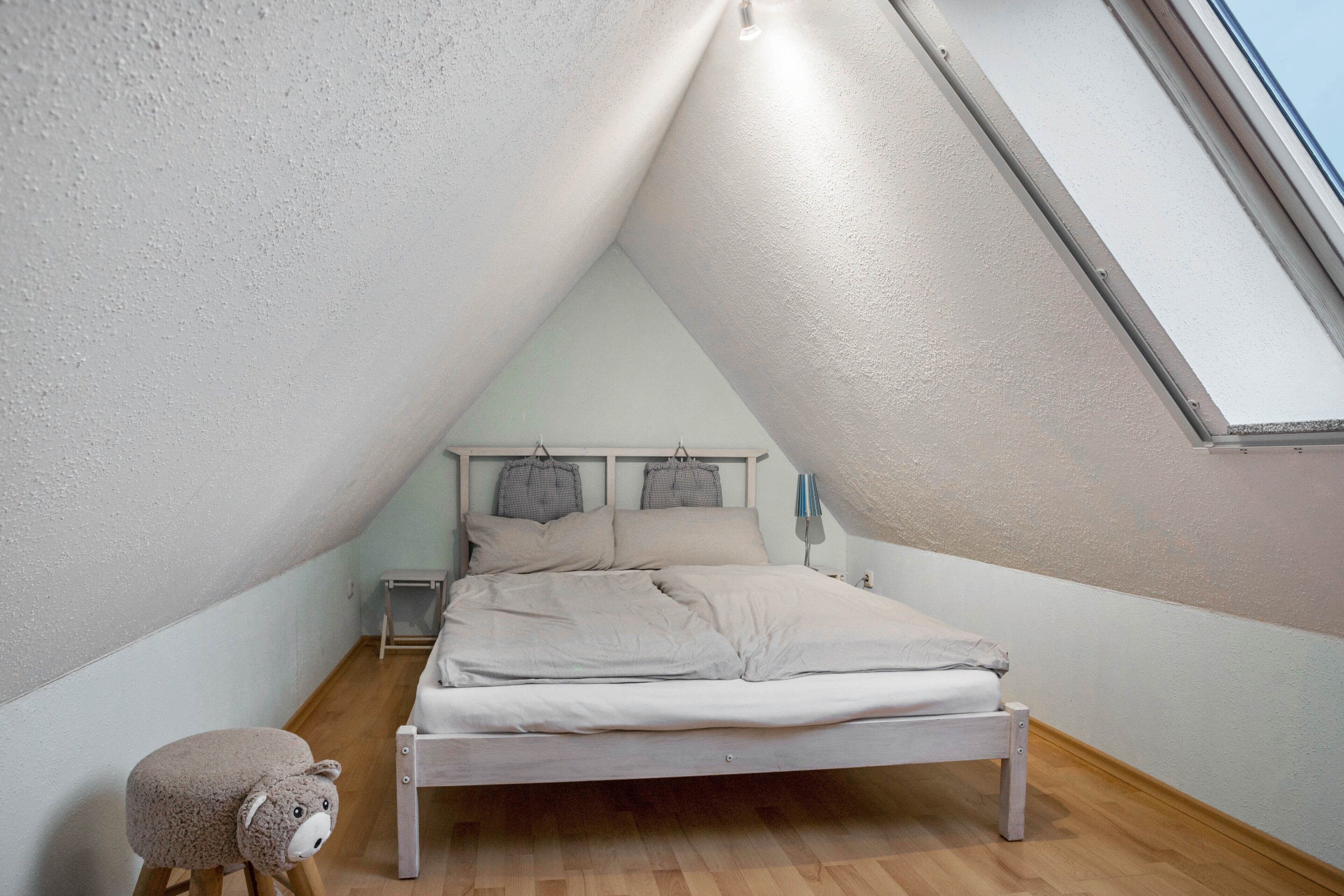 Ein Schlafzimmer mit schrägem Dach, einem Bett, einem kleinen Hocker und einem Nachttisch.