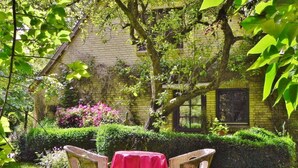 A garden with a table and chairs, a brick building, and lush greenery. - Holiday Apartment Mulleby with Shared Garden and Wi-Fi (Süderhackstedt)