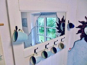 Une pièce avec une fenêtre, une étagère fixée au mur où sont posées des tasses, et un élément décoratif mural.