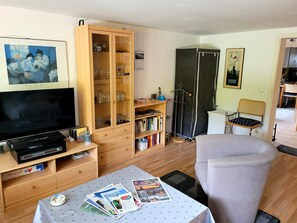 Un salon comprenant un téléviseur, un meuble en bois, une bibliothèque et un coin repas avec une chaise.