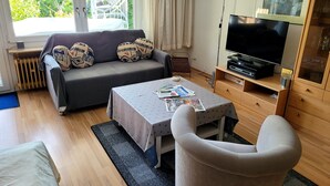 Un salon avec un canapé, une table avec des magazines, un téléviseur et un meuble en bois.