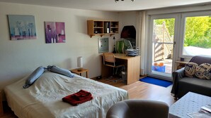 Une pièce comprenant un lit, un bureau, une chaise et un canapé. Il y a des tableaux au mur, une fenêtre et une porte.