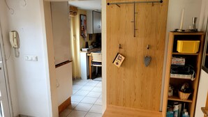 Une pièce avec une armoire en bois, un coin cuisine à l’arrière-plan et une étagère contenant divers objets.