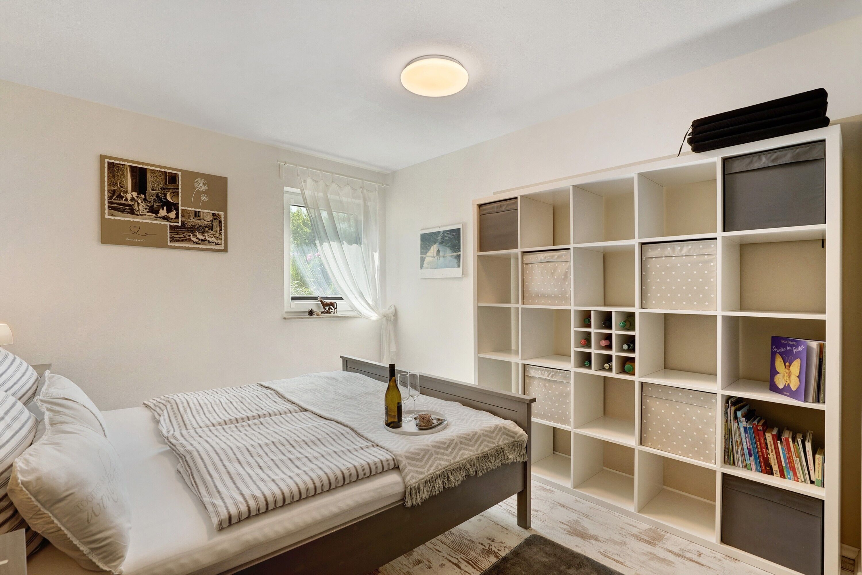 A bedroom with a bed, a bookshelf, and a window with curtains.