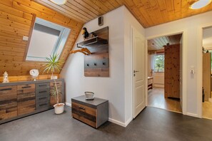 A modern interior with a wooden ceiling, a built-in shelf, a potted plant, a small cabinet, and a door leading to another room. - Apartment 'Micha's Ferienwohnung' with Private Terrace, Private Garden and Wi-Fi (Bredstedt)