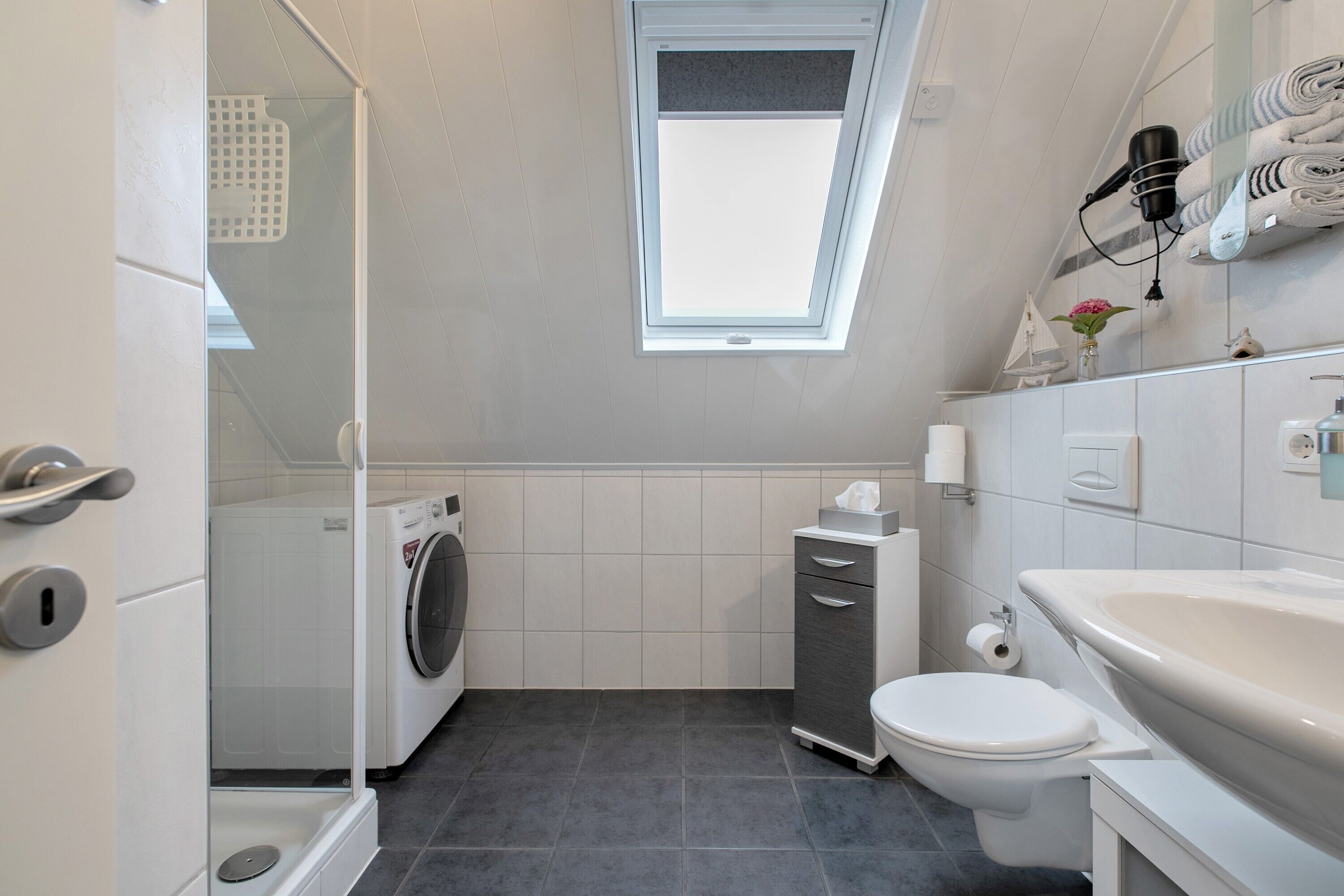Een moderne badkamer met dakraam, wasmachine, toilet en wastafel.