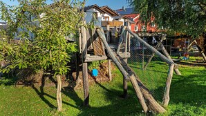 A wooden play structure in a grassy area with a house in the background.