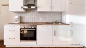 A modern kitchen with white cabinetry, a built-in oven, a coffee maker, and a stainless steel range hood.