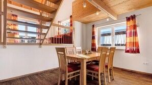 Un espace repas avec une table et des chaises en bois, un escalier et de grandes fenêtres avec des rideaux.