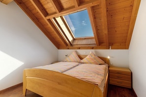 A bedroom with a sloped ceiling, a skylight, a bed with striped bedding, a bedside table, and a nightstand. - Apartment 'Ferienwohnung Apfel' with Shared Garden, Balcony and Wi-Fi (Appenweier)