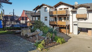 Un immeuble résidentiel doté de nombreux balcons, d’un jardin agrémenté d’une brouette en bois et d’une antenne parabolique.