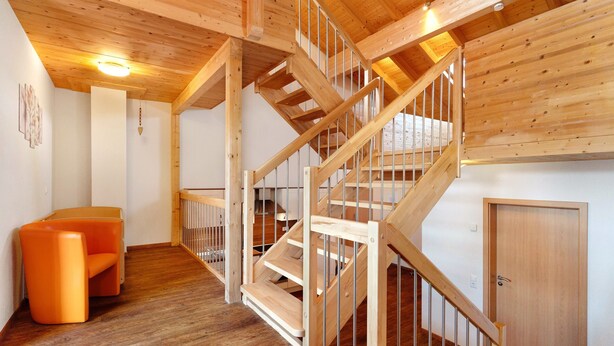 A wooden staircase with a metal railing, a wooden door, and a small orange chair in a room with wooden flooring and walls. - Apartment 'Ferienwohnung Mirabelle' with Shared Garden, Balcony and Wi-Fi (Appenweier)