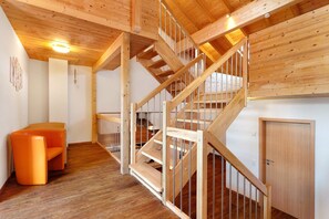 A wooden staircase with a metal railing, a wooden door, and a small orange chair in a room with wooden flooring and walls.