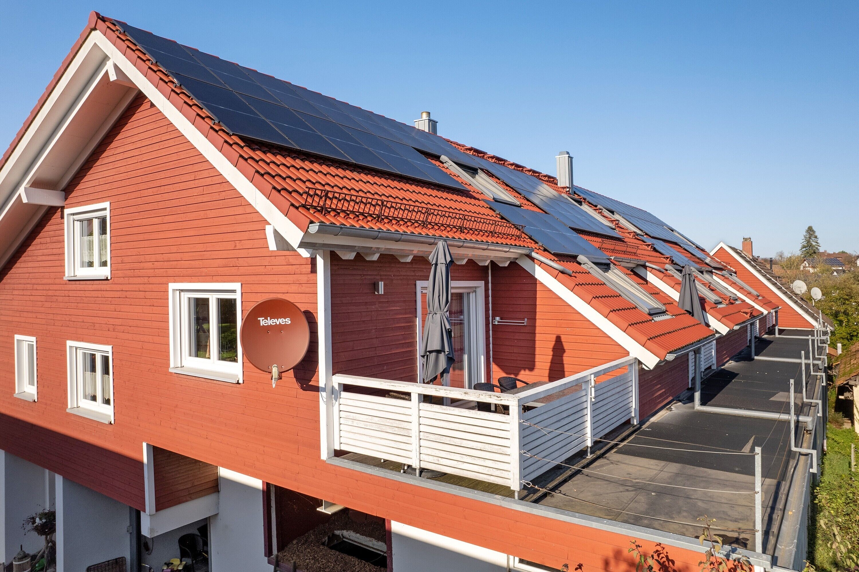 Un edificio de techos rojos con paneles solares, una antena parabólica y un balcón.