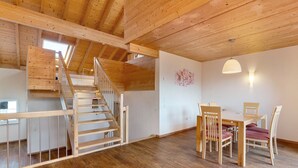 Un intérieur en bois avec un escalier, un coin repas avec des chaises et un mur agrémenté d’un luminaire.