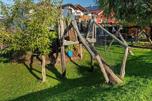 A wooden play structure in a grassy area with a house in the background.
