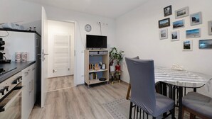 Kompakti keittiö, jossa on jääkaappi, mikroaaltouuni ja liesi, ruokailutila pöydän ja tuolien kera sekä seinä, jossa on kehystettyjä kuvia.