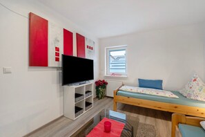Ein Zimmer mit einem Bett, einem Fernseher, einem Fenster und einer roten Blumenkomposition.