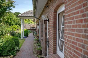 A brick house with a covered porch, a garden with potted plants, and a pathway leading to the house.