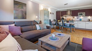 A modern living room with a sofa, coffee table, and dining area with chairs and a table. - Apartment 'Fewo Birkenallee - Lavendel' with Private Terrace (Deinste)
