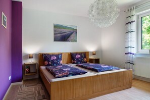 Un dormitorio con cama de madera, dos mesitas de noche, una lámpara de pared, una luz de techo y una ventana con cortinas.