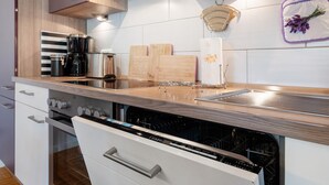 A modern kitchen with a built-in dishwasher, wooden countertop, and a coffee maker. - Apartment 'Fewo Birkenallee - Lavendel' with Private Terrace (Deinste)