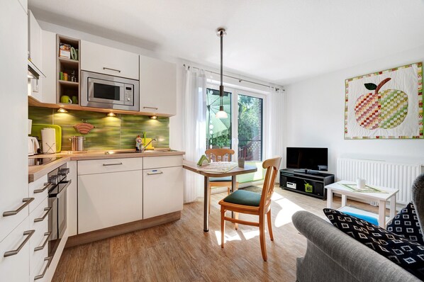 A modern kitchen with a microwave, wooden cabinets, and a dining area with a chair and table.