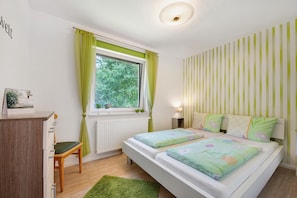 Een slaapkamer met een bed, een bureau, een stoel, een radiator en een raam met gordijnen.