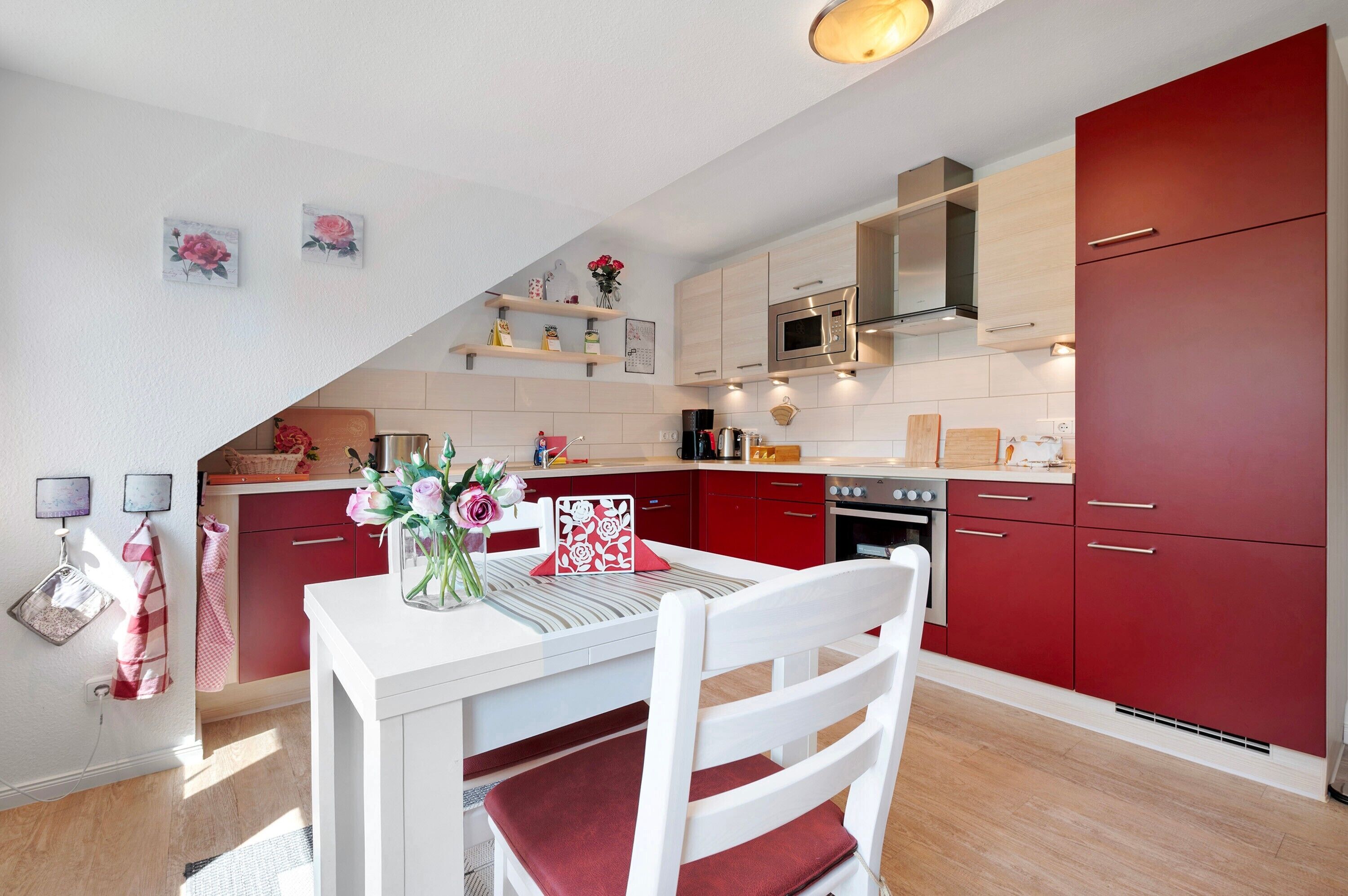 A modern kitchen with red cabinets, a white dining table, and a chandelier.