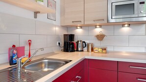Een moderne keuken met een RVS spoelbak, rode kastjes, een magnetron en een koffiezetapparaat.