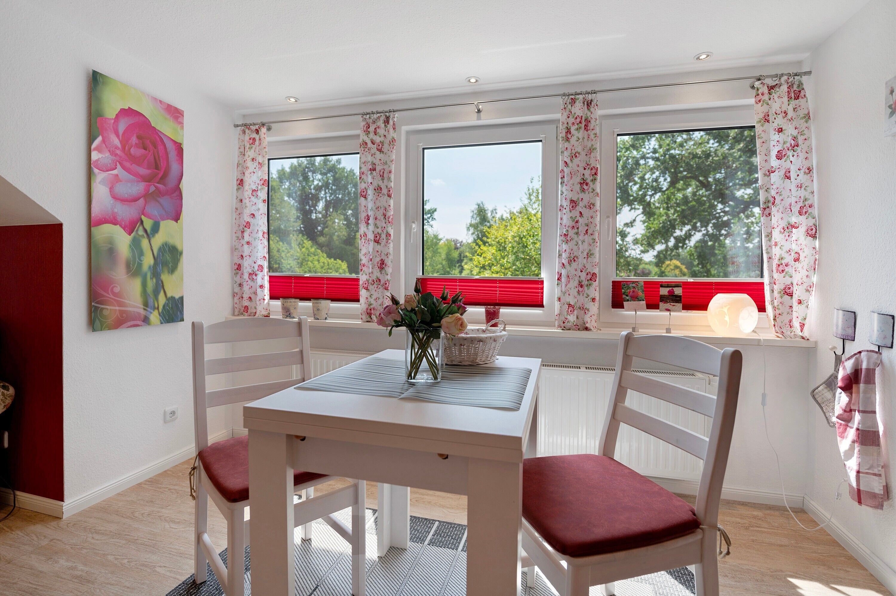 A dining area with a table and chairs, a vase with flowers, and a window with curtains.