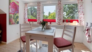 Een eethoek met een tafel en stoelen, een vaas met bloemen en een raam met gordijnen.