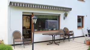 Een terras met een tafel, stoelen, een lamp en een raam met gordijnen.