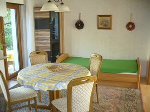 Ein Zimmer mit einem runden Tisch, vier Stühlen, einem grünen Sofa, einem gemusterten Teppich und zwei Wandbildern.