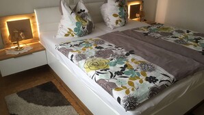 Een bed met bloemenbedekking, nachtlampjes en een nachtkastje van hout.