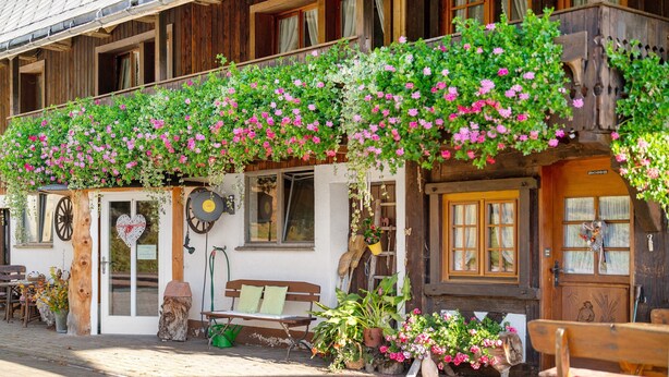 Un edificio in legno con un balcone fiorito, una panchina e una porta decorata con un cuore.