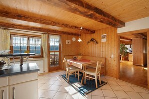 A wooden interior with a dining table, chairs, a kitchen area, and a view through a window.